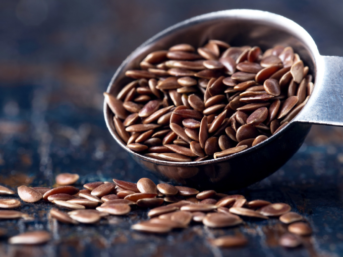 Braune Leinsamen, eine Art kleine Darmkur, liegen verstreut neben einem Teelöffel